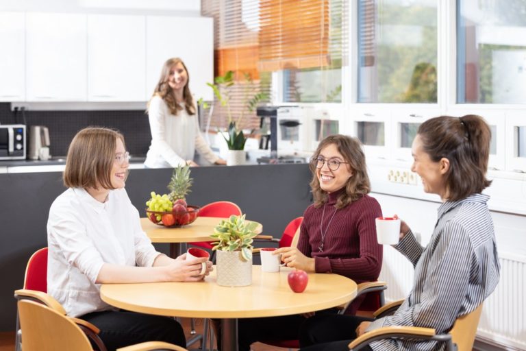 A group of coworkers sit at a table in a break room.