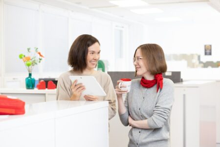 Nainen näyttää työkaverilleen tietoa tabletilta toimistoympäristössä ja molemmat hymyilevät.