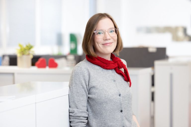 A woman stands in an office and smiles.